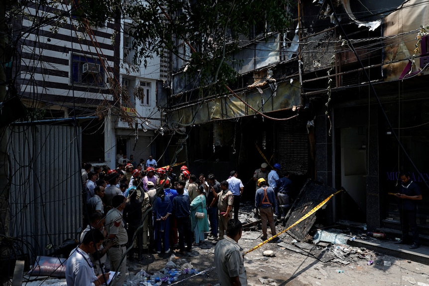 People wearing helmets stand around outside a burnt building.
