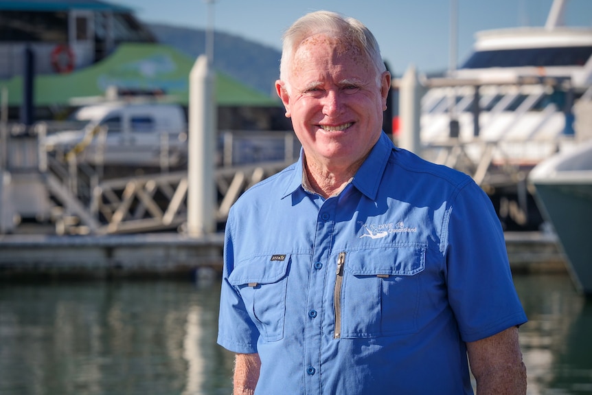 Terry Cummins stands on a jetty with boats behind him.