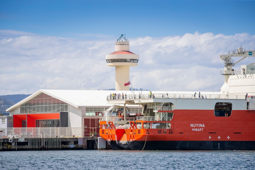A large orange and white icebreaker Antarctic research vessel at a port.