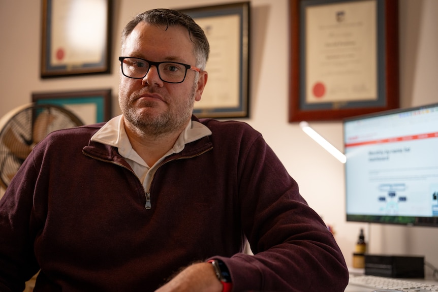 Man with glasses sitting at a desk, back turned from his computer