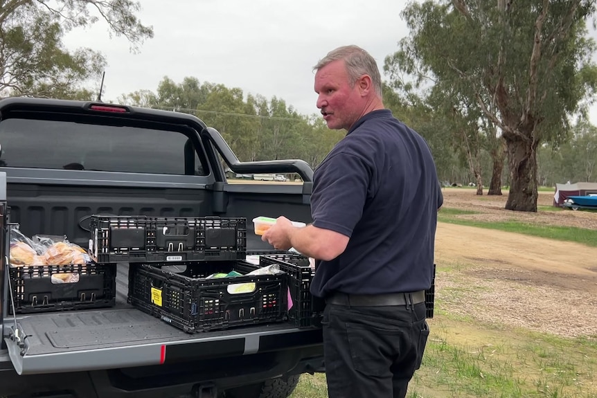 man organises trays of food out of the back of a ute