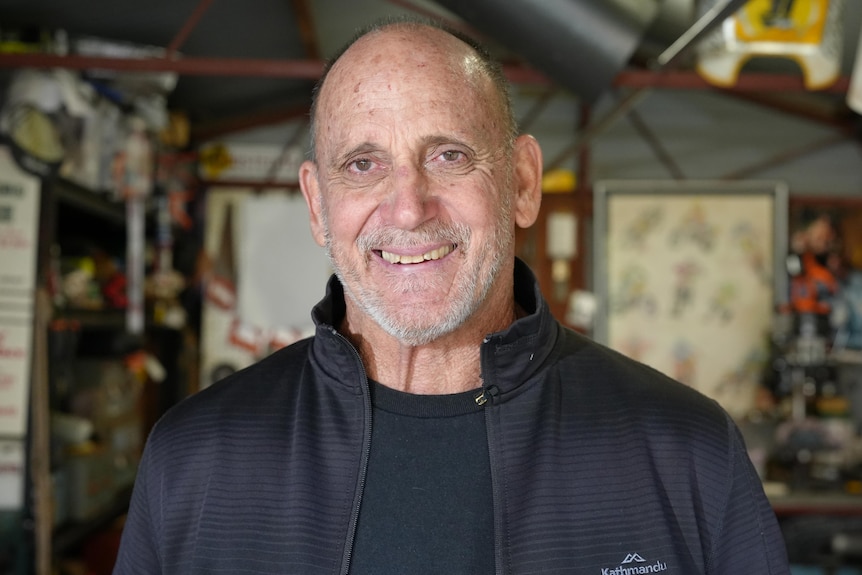 A bald man wearing a black jacket and shirt smiles at the camera. You can see him from the shoulders up.