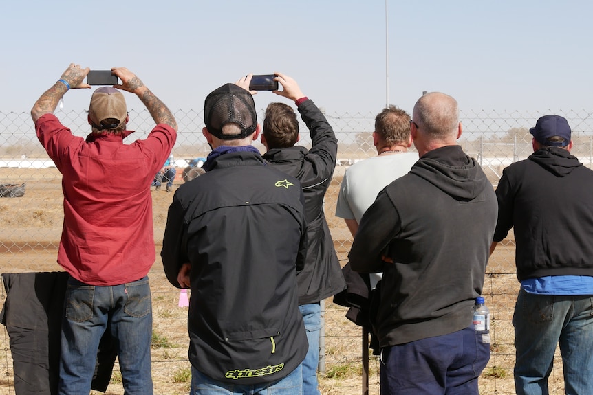 Spectators take photos of cars racing in the desert