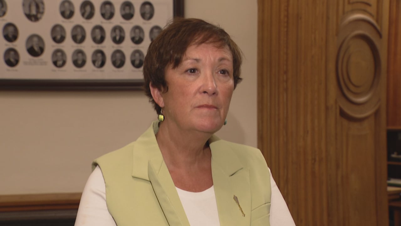 A dark haired woman wearing a light green vest, standing in a legislative building.