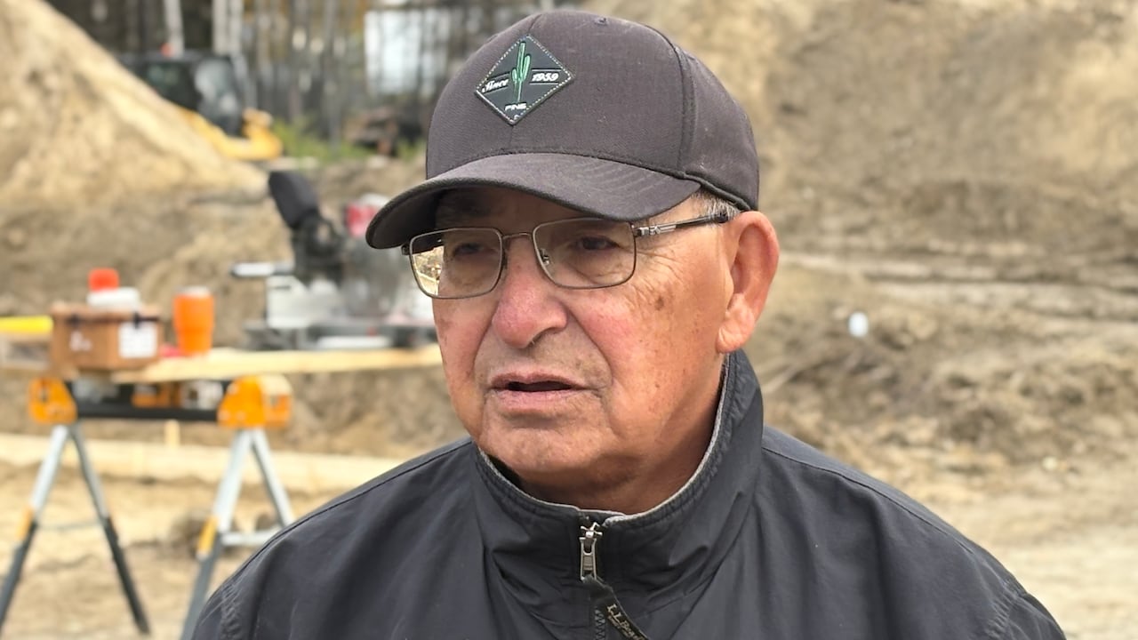 A man in a ball cap and glasses speaks to a reporter who is off camera during an interview outdoors.