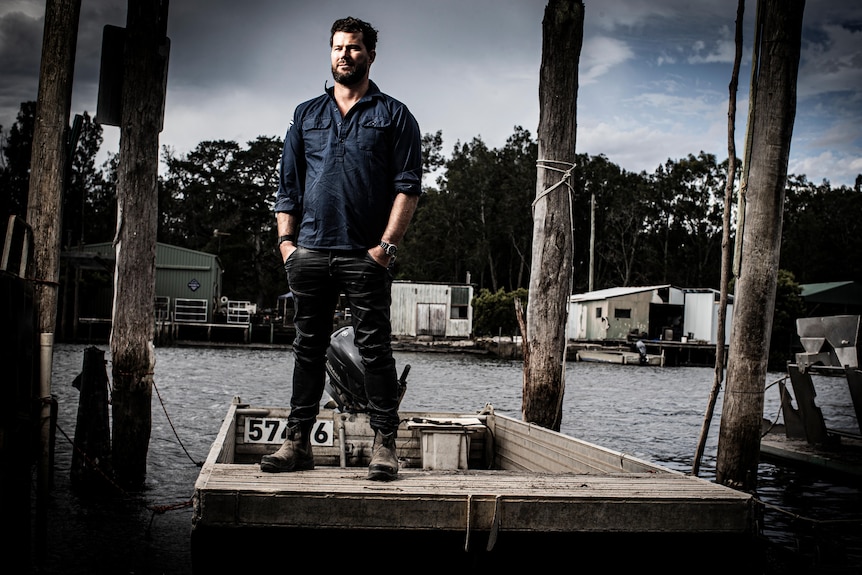 Male oyster farmer standing on a jetty with his hans in his pockets.