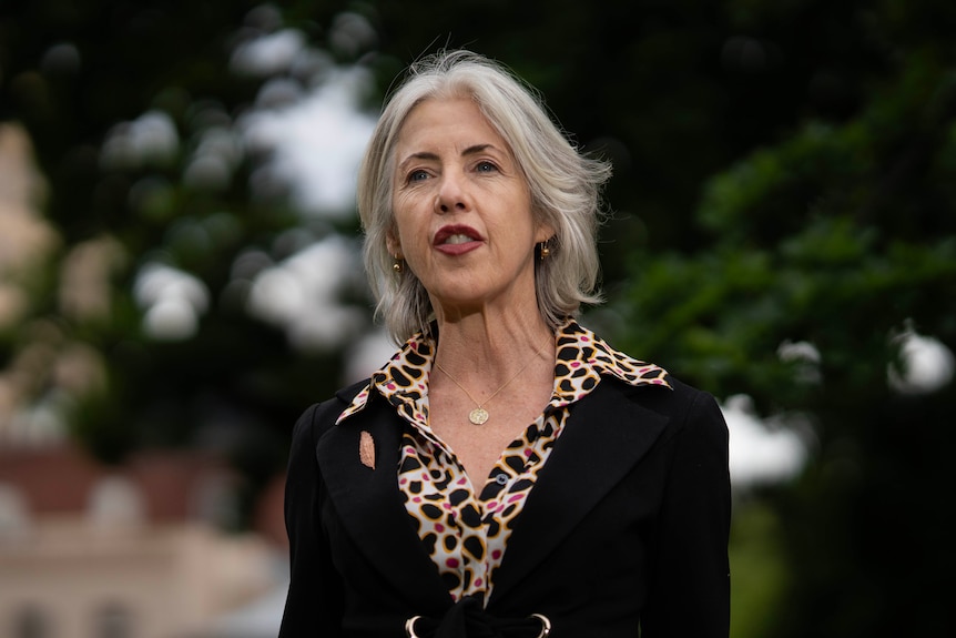 A lady with short white hair standing outside of parliament.