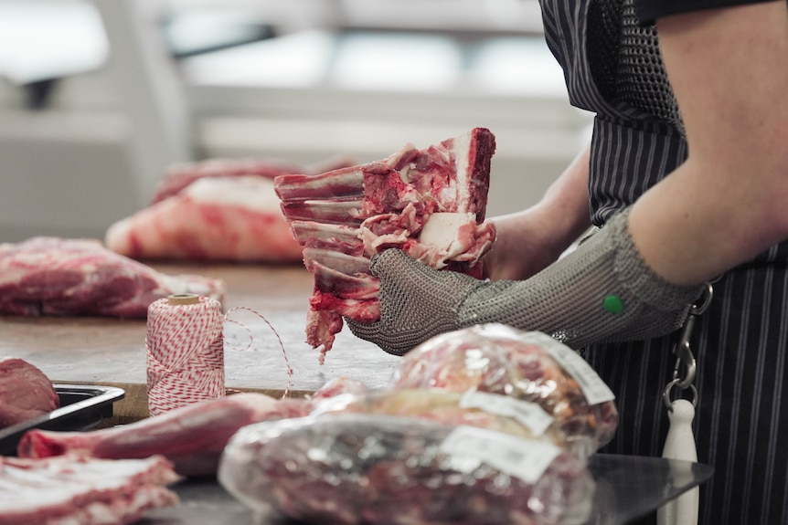 Blonde woman wearing hat and apron working in a butchers kitchen.