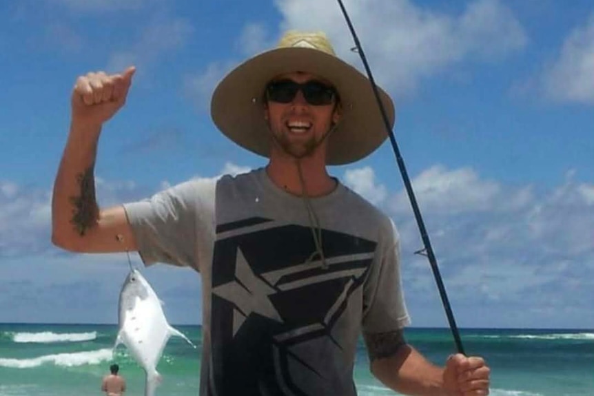 A man holding a fishing rod and fish on a beach.