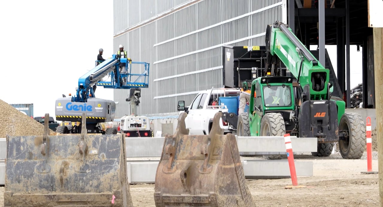 Two mechanical lifts are used by construction workers on the exterior of a building.