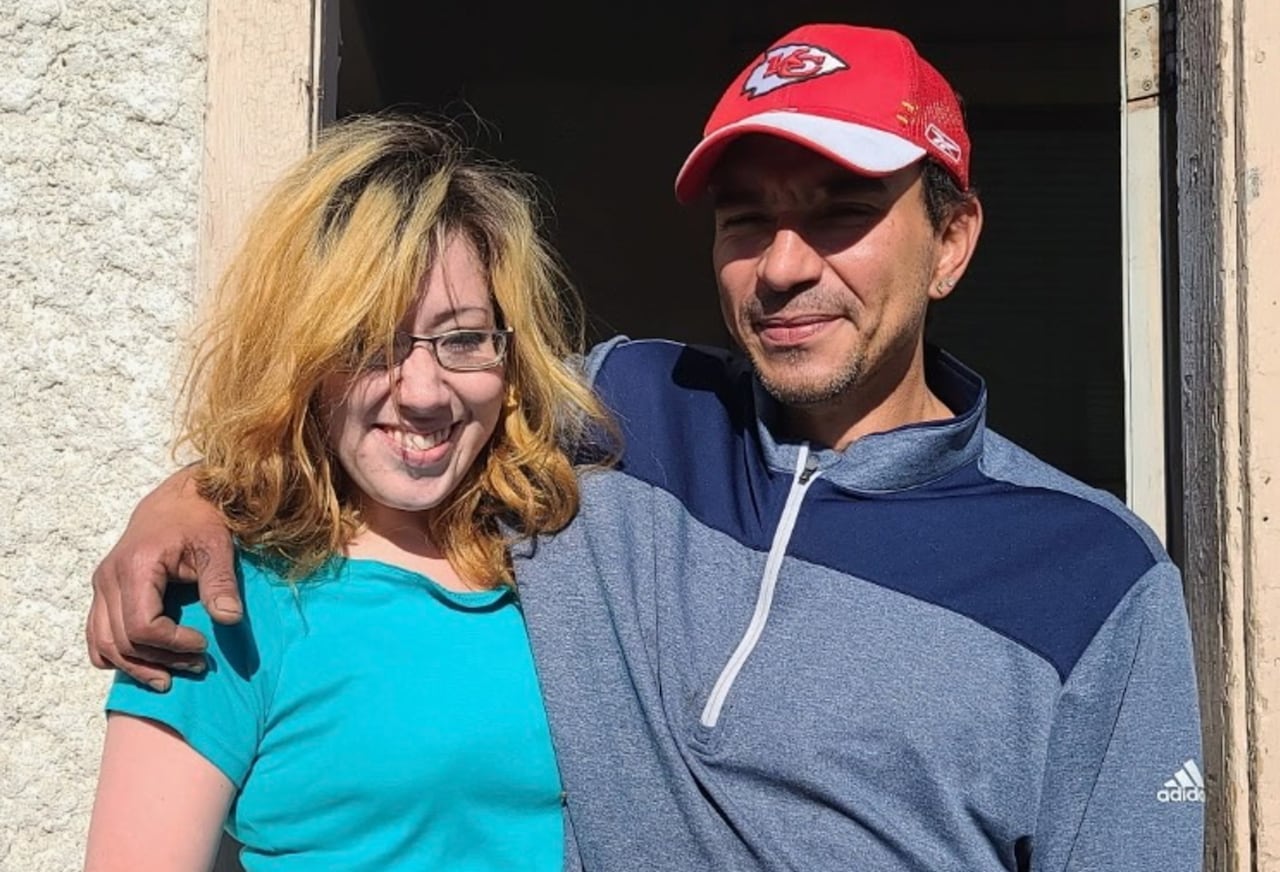 A man and a woman stand in front of a house.