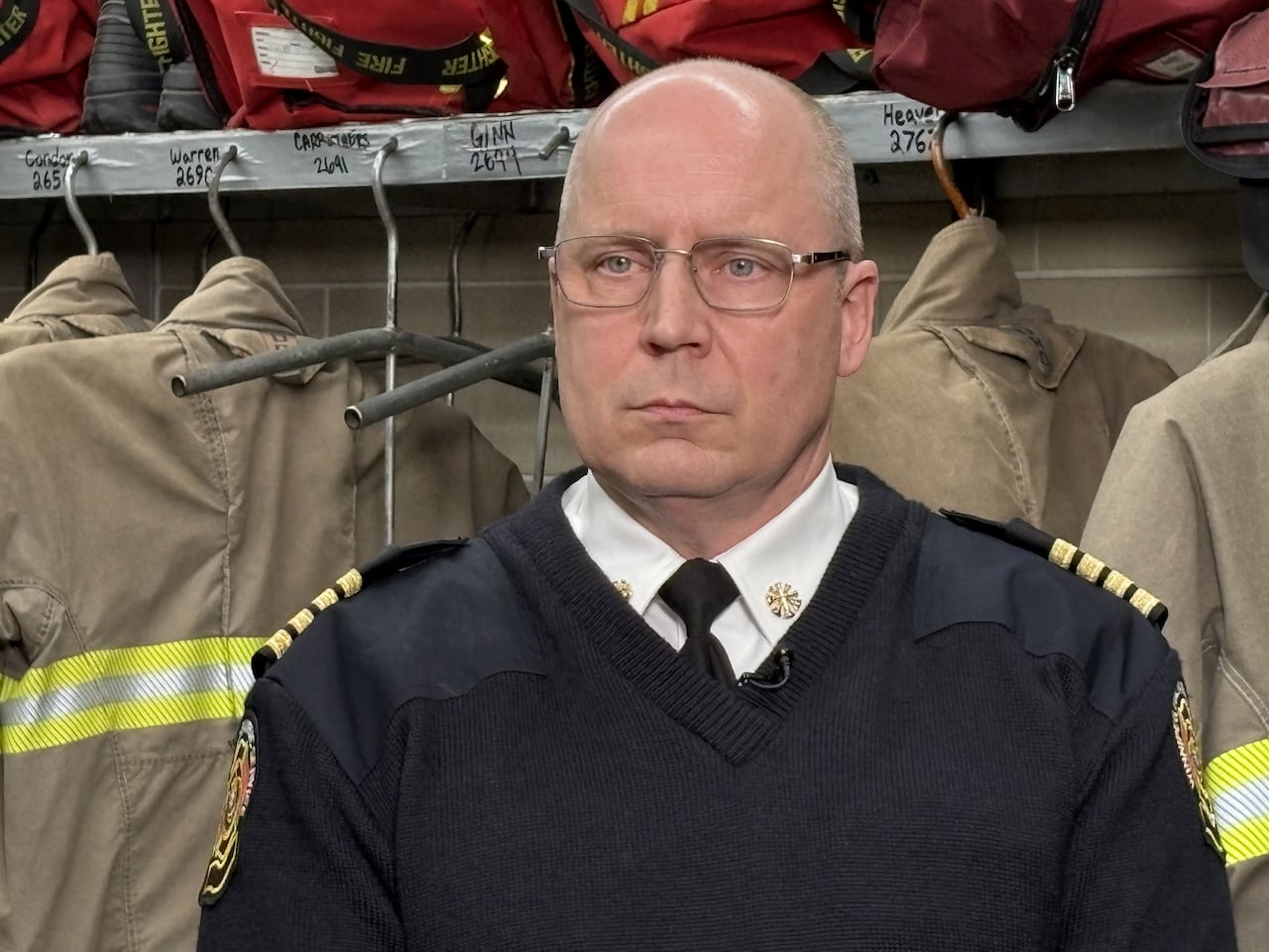 A man in glasses standing with firefighter uniforms around him.