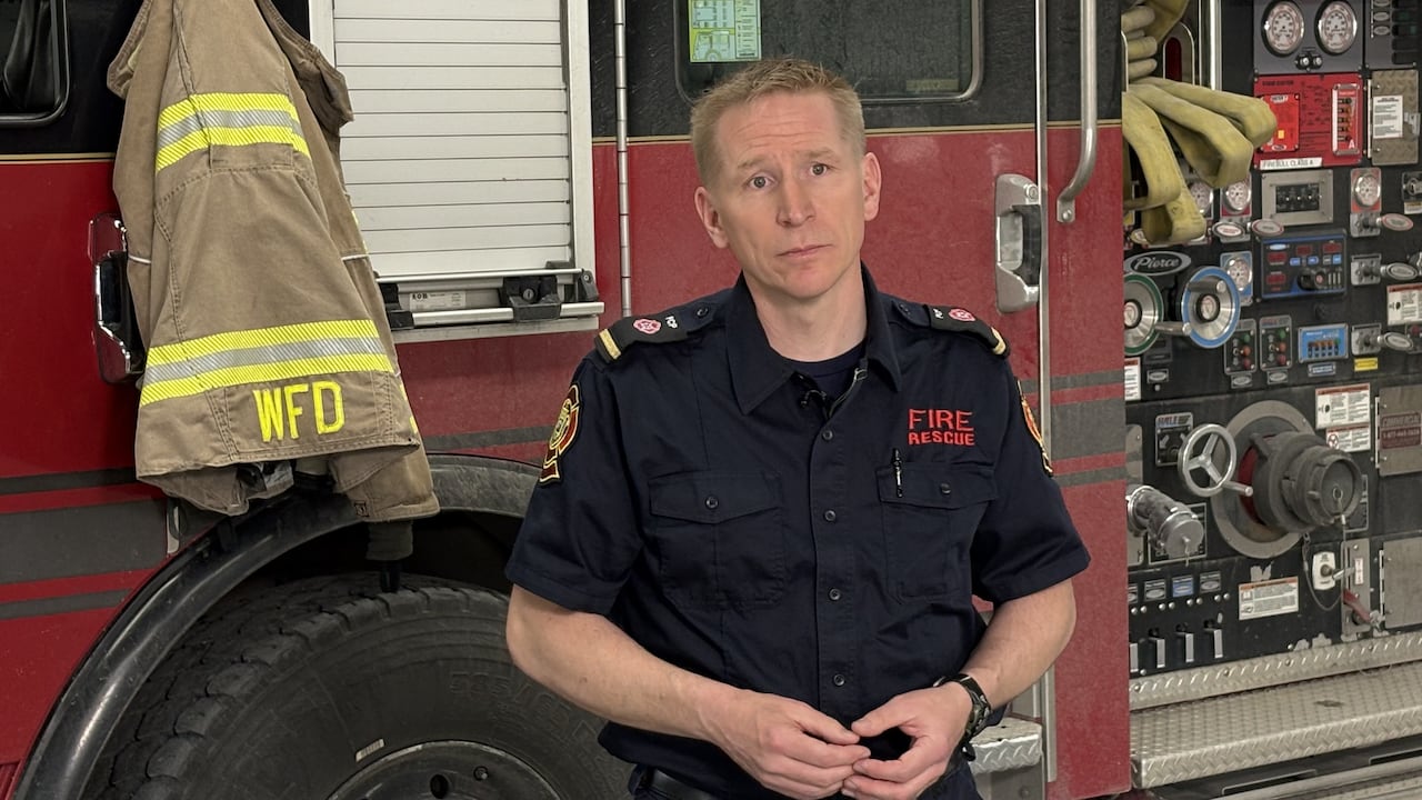 A man in a firefighter uniform stands in front of a firetruck.