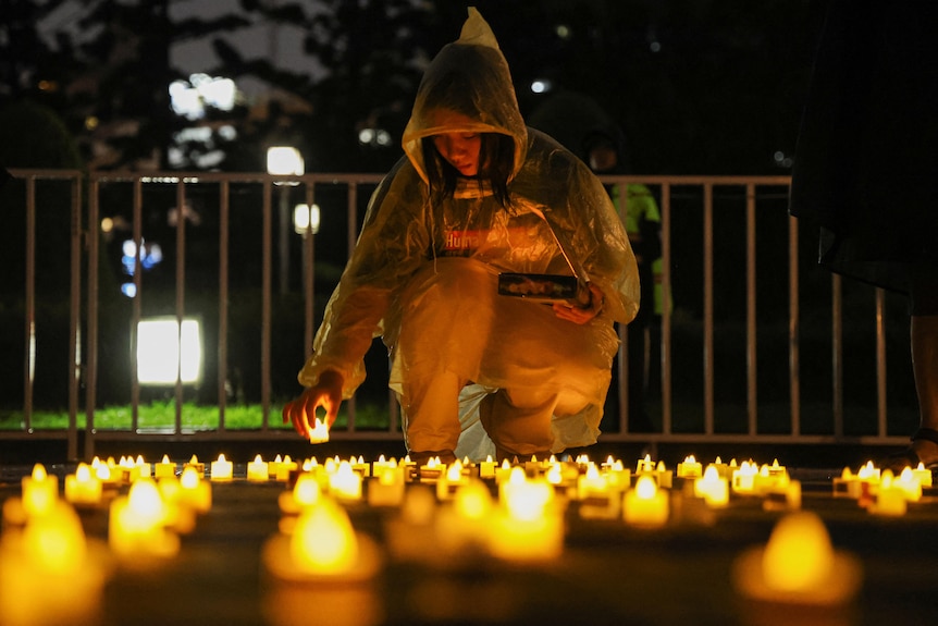 A woman puts a candle on the ground among other candles.