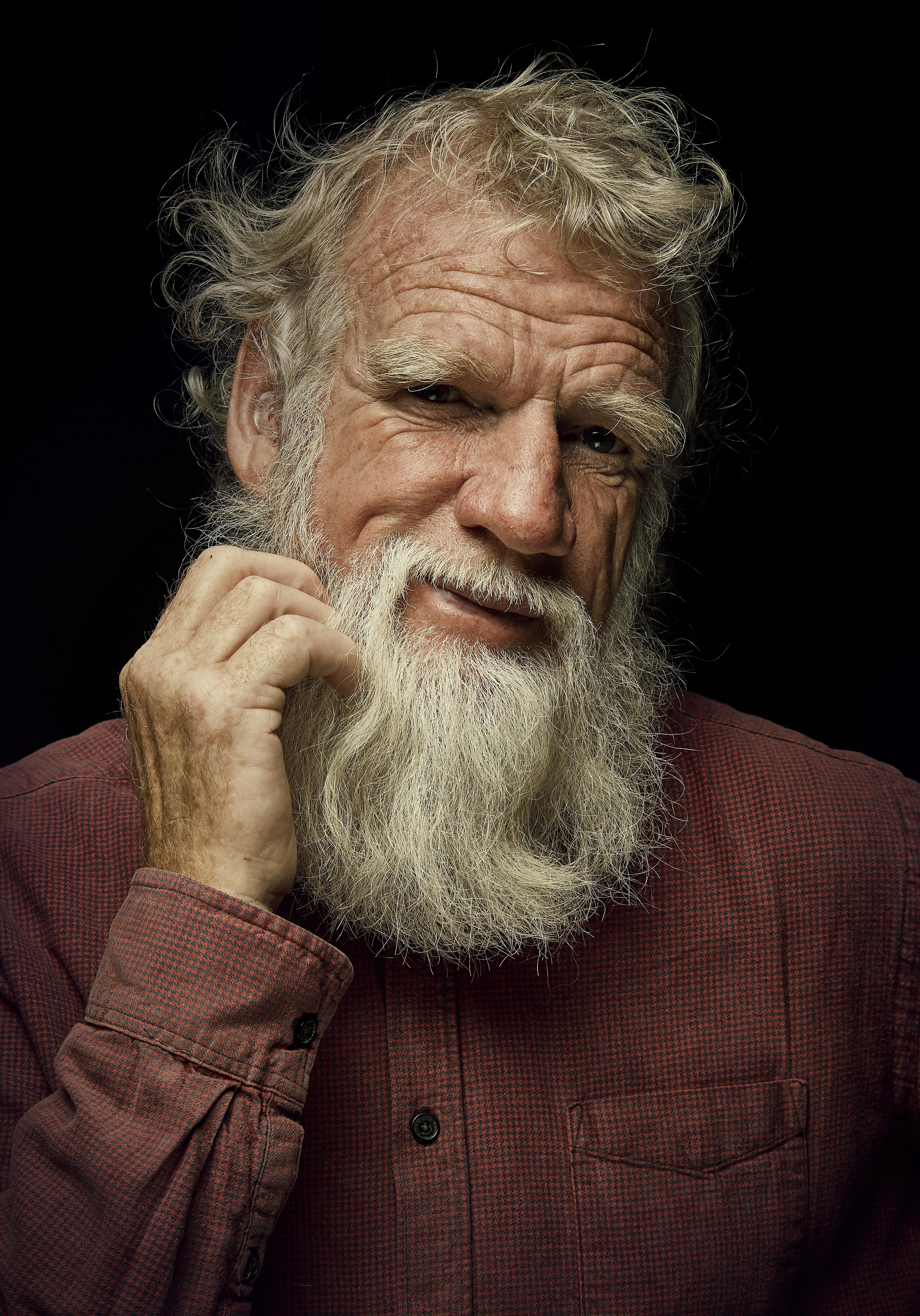 A man with grey hair and beard looks at the camera with a serious expression.