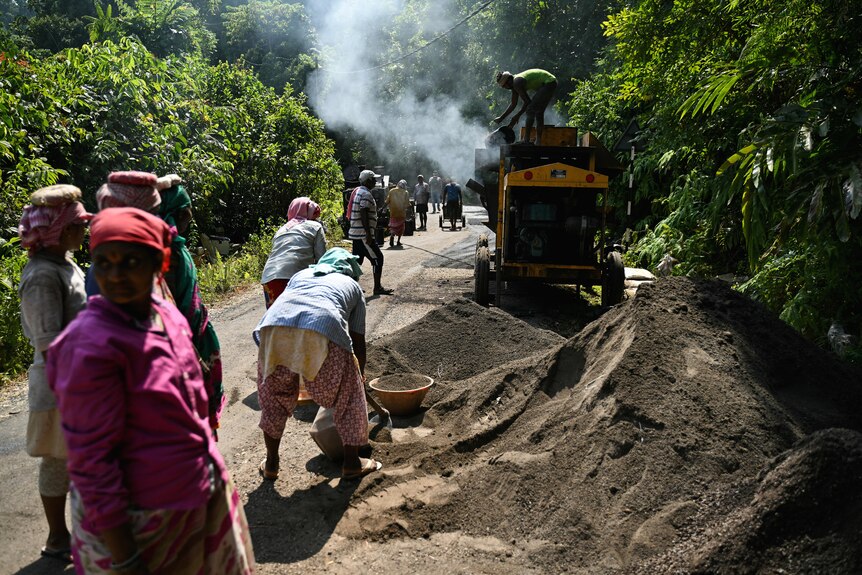Dozens of people work to build a road through thick forest using a machine that's spewing smoke