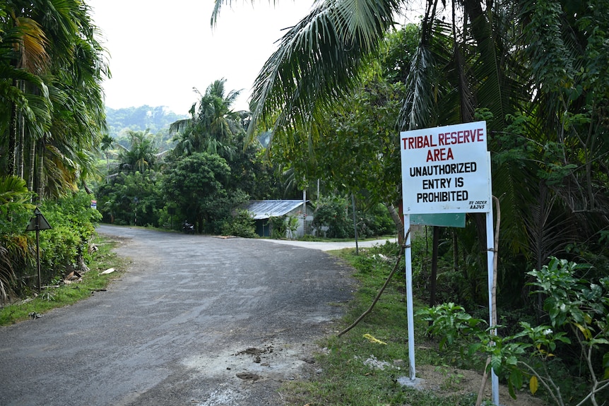 A sign stating 'tribal reserve area' and that unauthorised entry is not allowed with a small hut and dense forest behind it