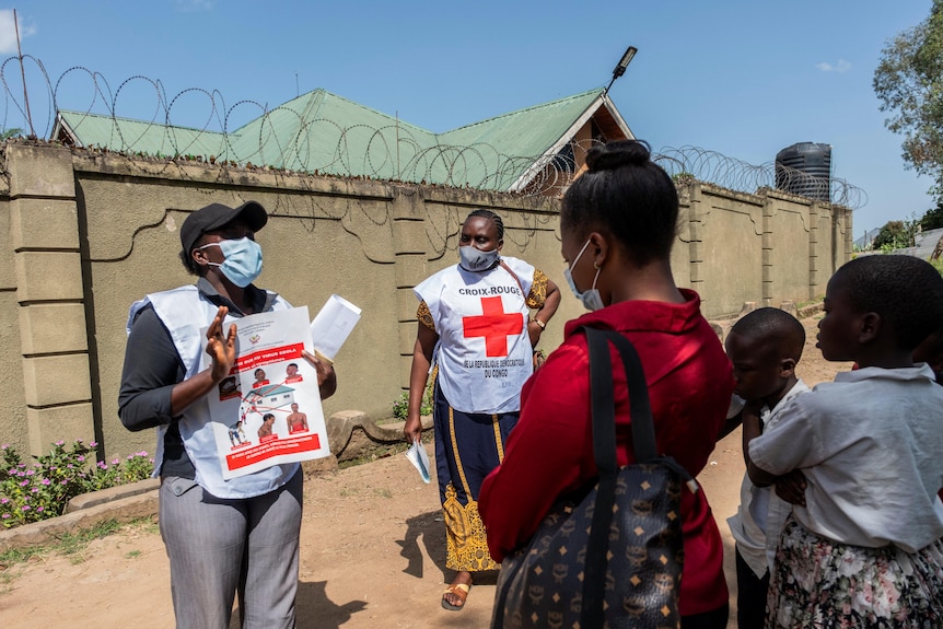 A woman in a red cross vest holds up a sign explaining Ebola to civilians.