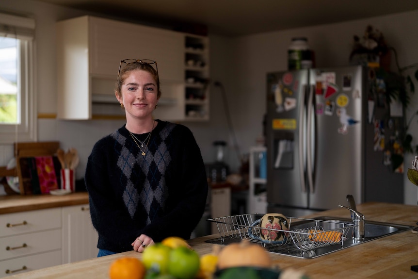 Young women leans on her kitchen bench, posing for photo