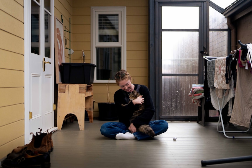 Young woman sits on the floor holding a fluffy brown cat