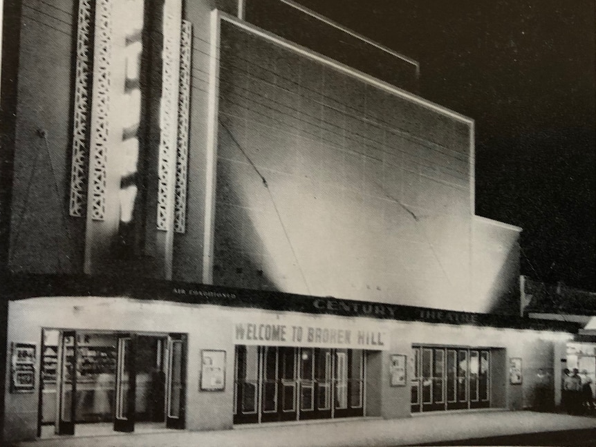 An old black and white photo of an art deco building lit up with bright lights 
