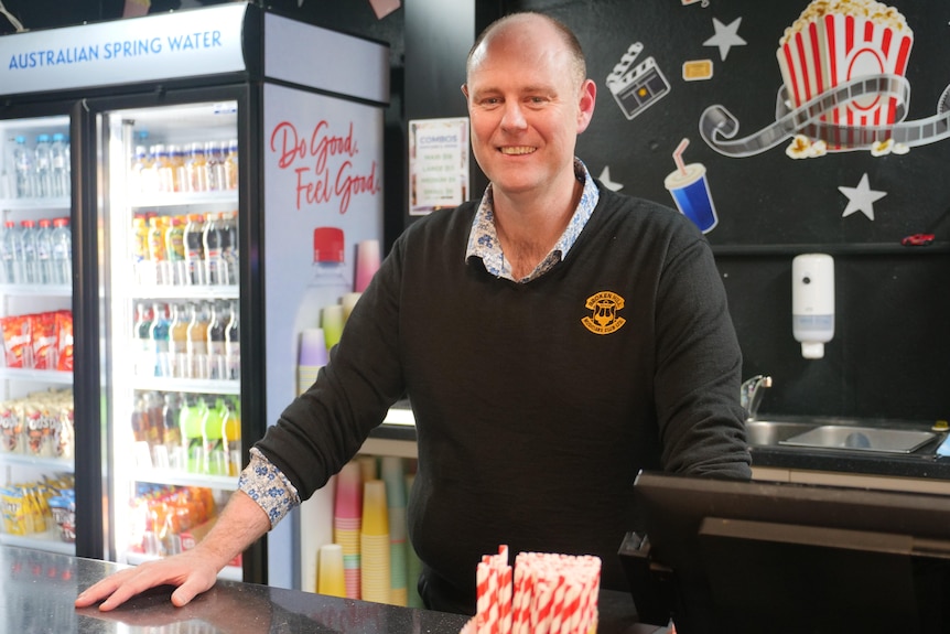 A man standing behind the counter at a cinema concession stand smiling at the camera