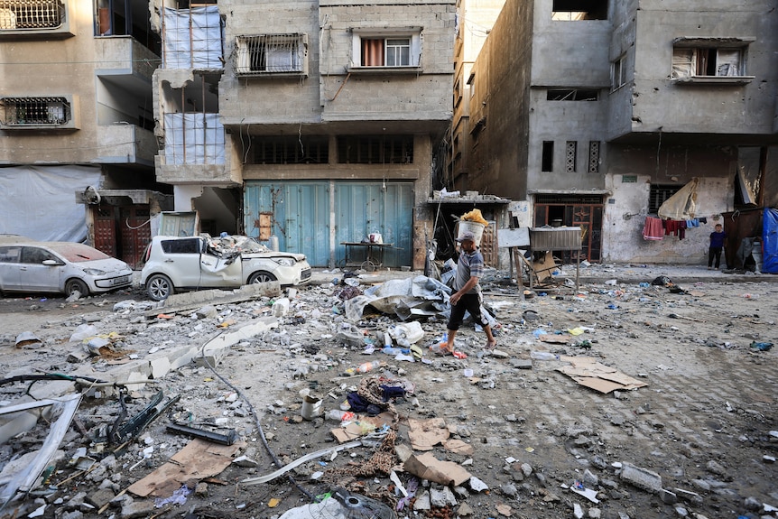 Rubble and destroyed buildings with a man walking on a road alongside squashed cars