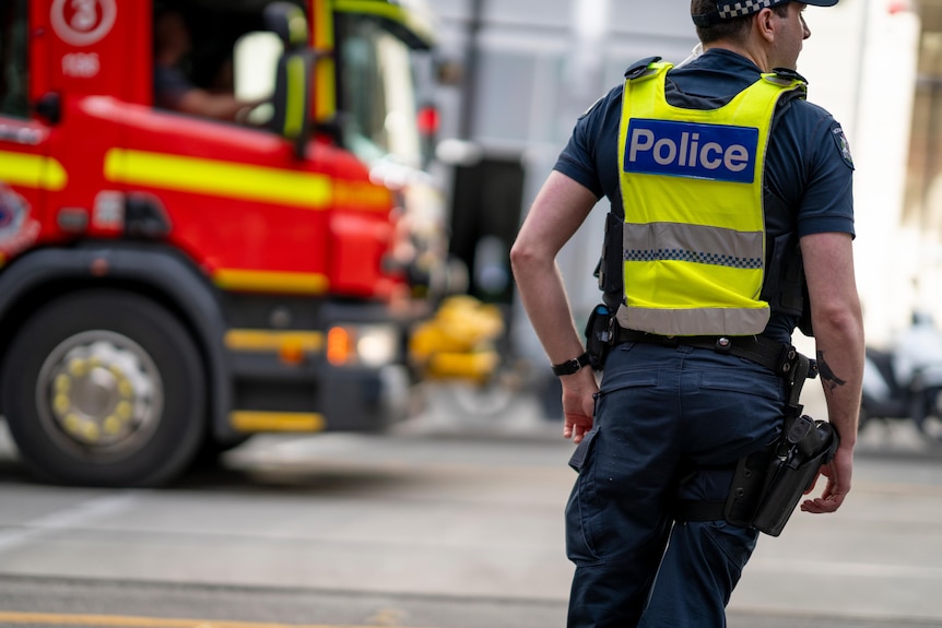 A Victoria Police officer stands next to a fire engine