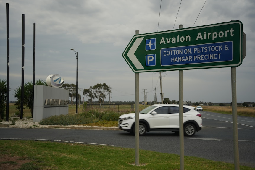 Road sign towards Avalon airport and precinct with car driving past.