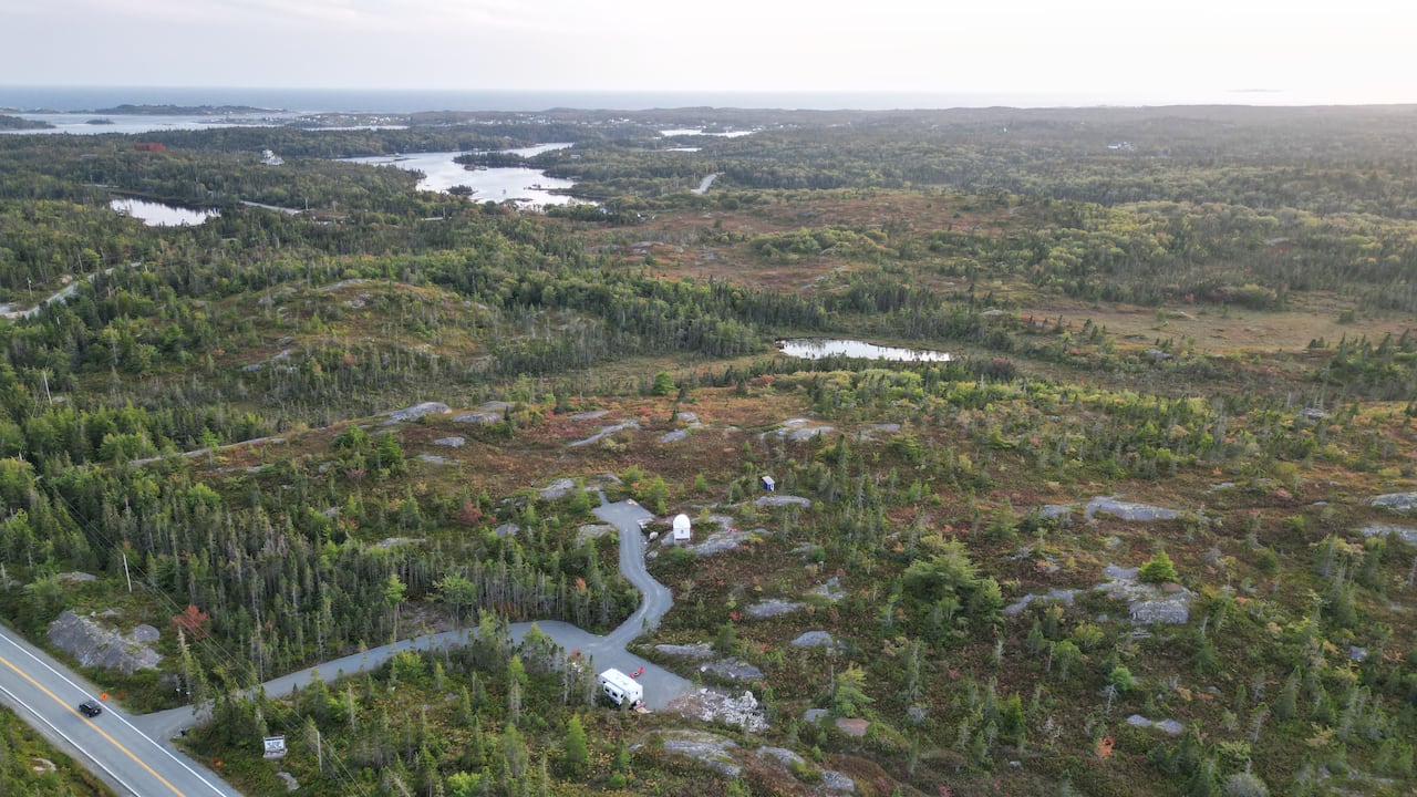 A green forested area is seen from the sky, with a road running along the bottom of the photo and small lakes in the distance.