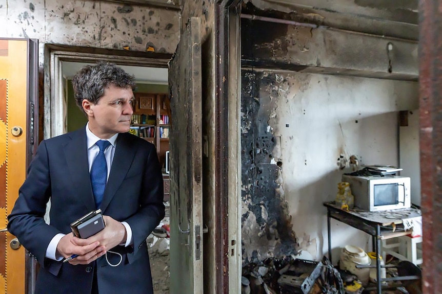 a man in a suit walks through a charred burnt out building - someone's home