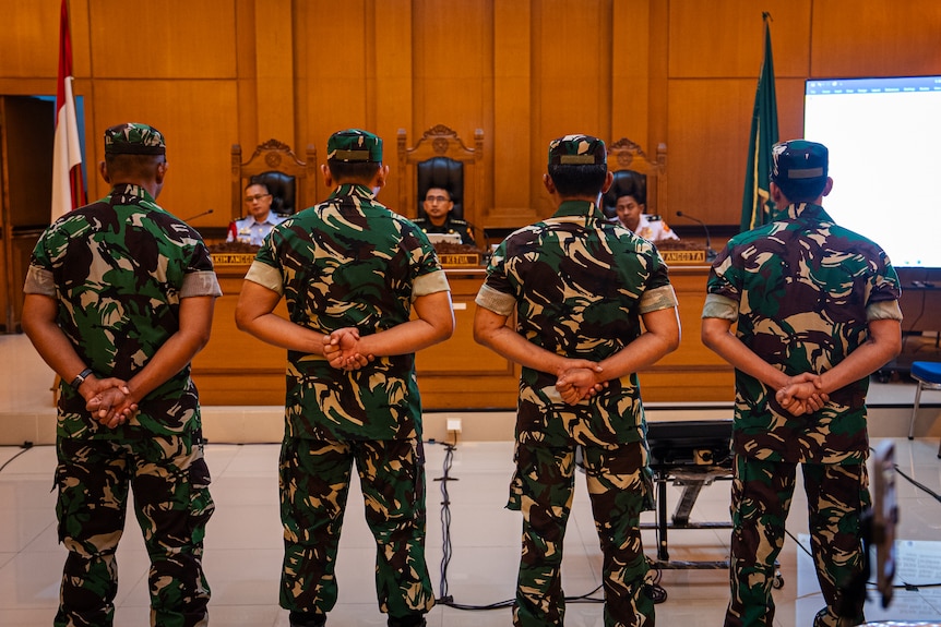 Four men dressed in military fatigues line up in front of a judge in Jakarta