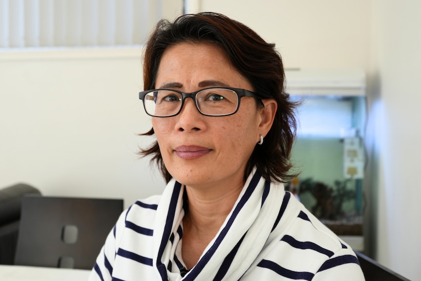  A Chinese woman with dark hair, glasses and a white stripy top looks at the camera. 