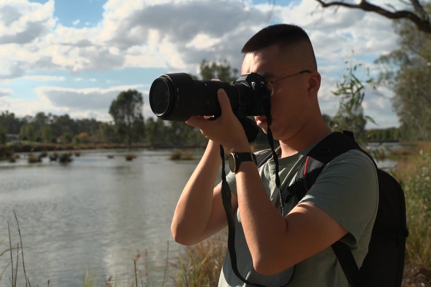 A man with a camera by a lake 