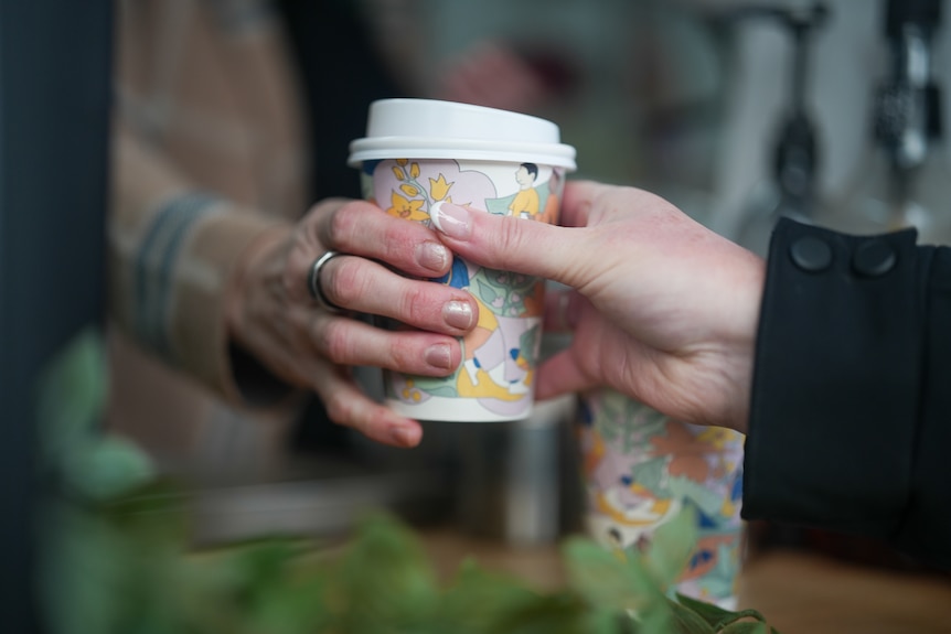 Close up shot of hands: Lee Brown's hand passing a coffee to another woman's hand over the counter