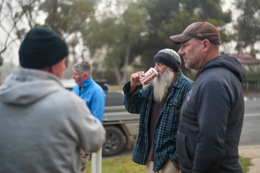 Four men standing by the side of the road holding and drinking coffees.