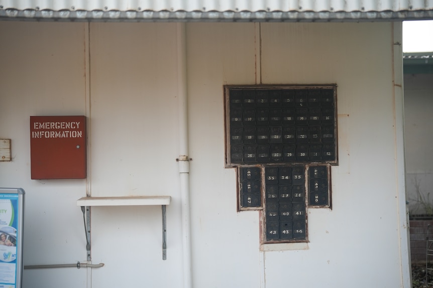 Outdoor wall of 50 post boxes, sheltered by tin roof.