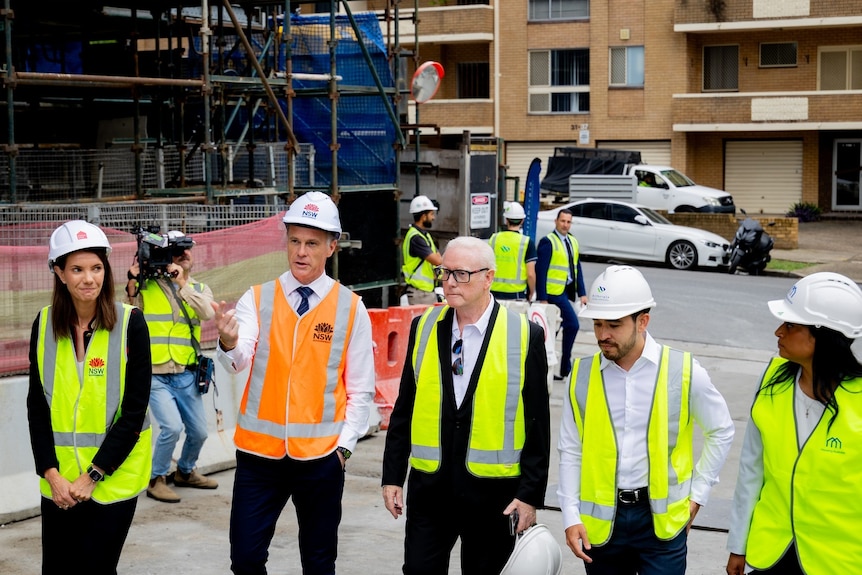 nsw mrem ier chris  minns with other m inisters and oificials wearing hard hats and high viz walking through a construction site