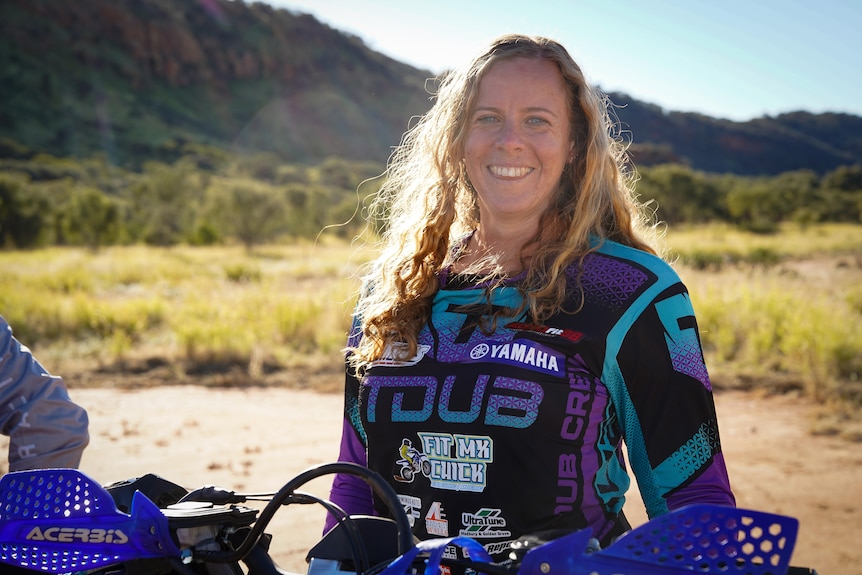 A woman in bike gear smiling at the camera. 