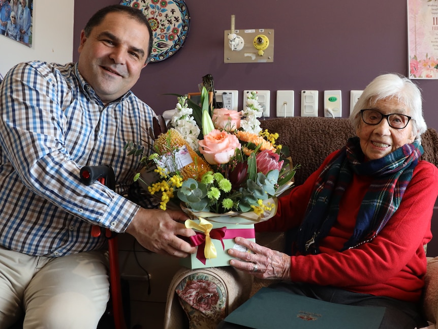 A man presents an elderly lady with flowers and a certificate on her 112th birthday 