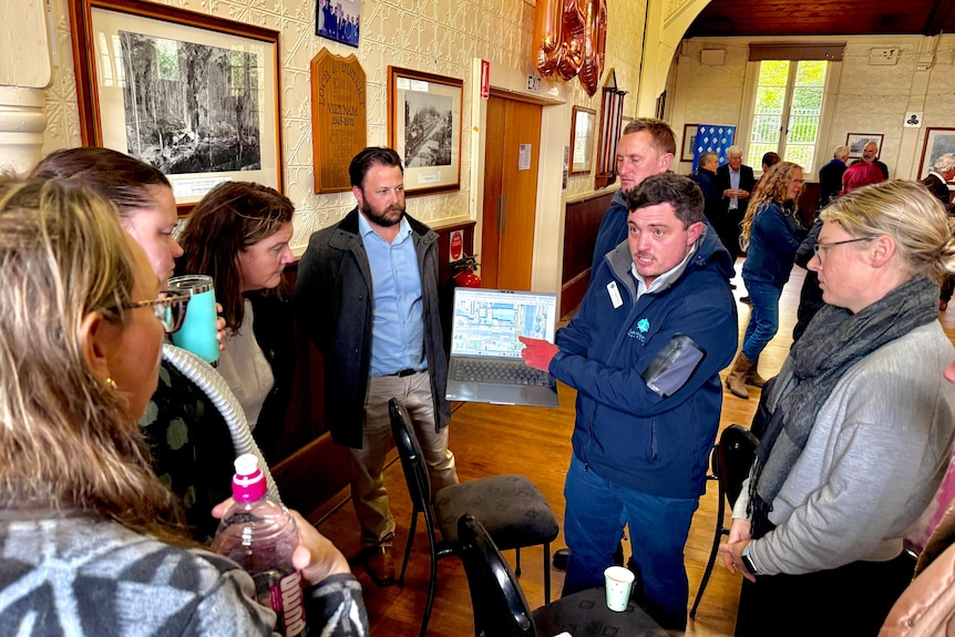 Image of a group of people inside a town hall, referring to a laptop with images of road safety upgrade plans on the screen. 