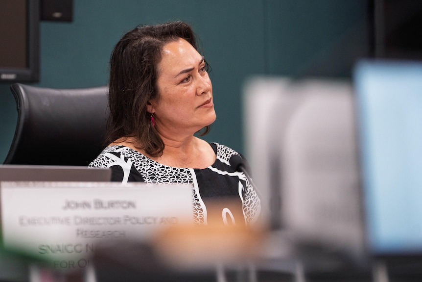A woman with dark hair wearing a serious facial expression.