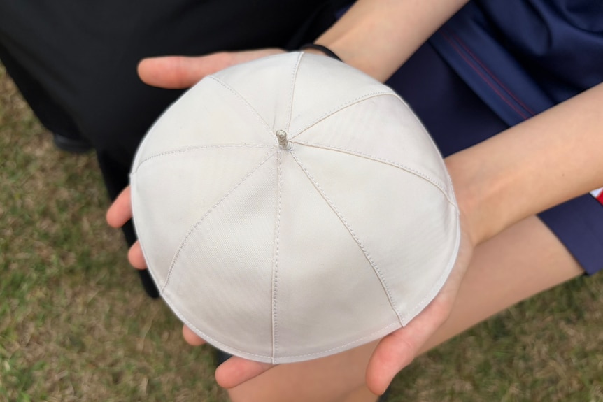 A small white dome hat in the hands of a child
