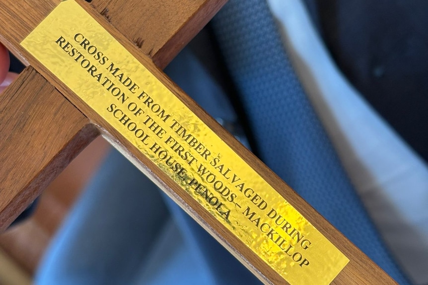 A wooden cross with a gold sticker plaque on it.