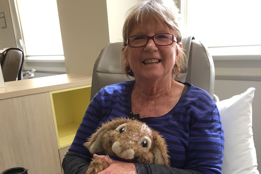 A woman in a blue shirt holding a stuffed rabbit toy and smiling at the camera.