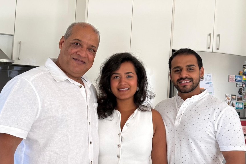 Sunil, Surbhi and Saransh Sharma smile, standing in a white kitchen.