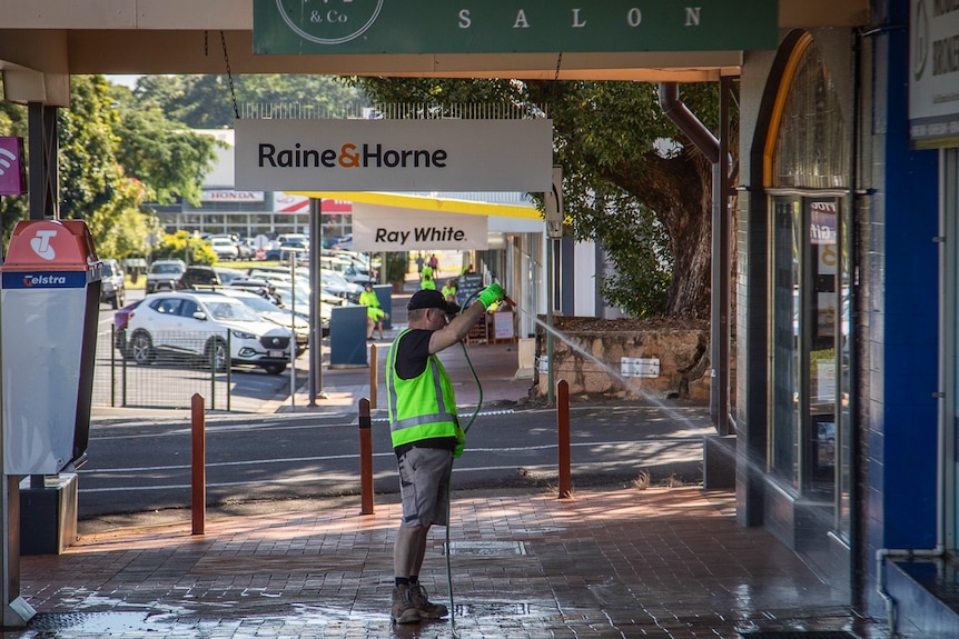 man holding hose spraying shop front and pavers with water