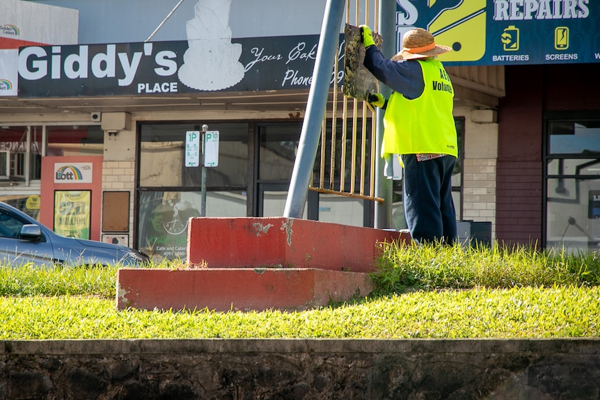 Woman in yellow high-vis vest cleaning sign on main street of small town