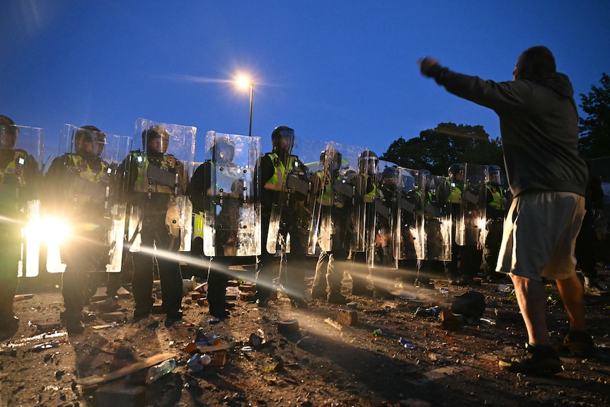 police with riot gear face off protestors in a street at night