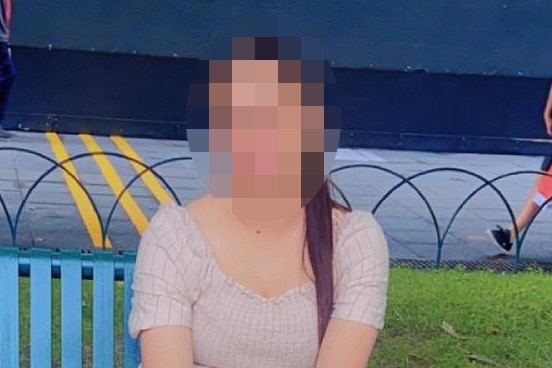 A woman whose face is pixelated wearing a dress on a bench in a park.